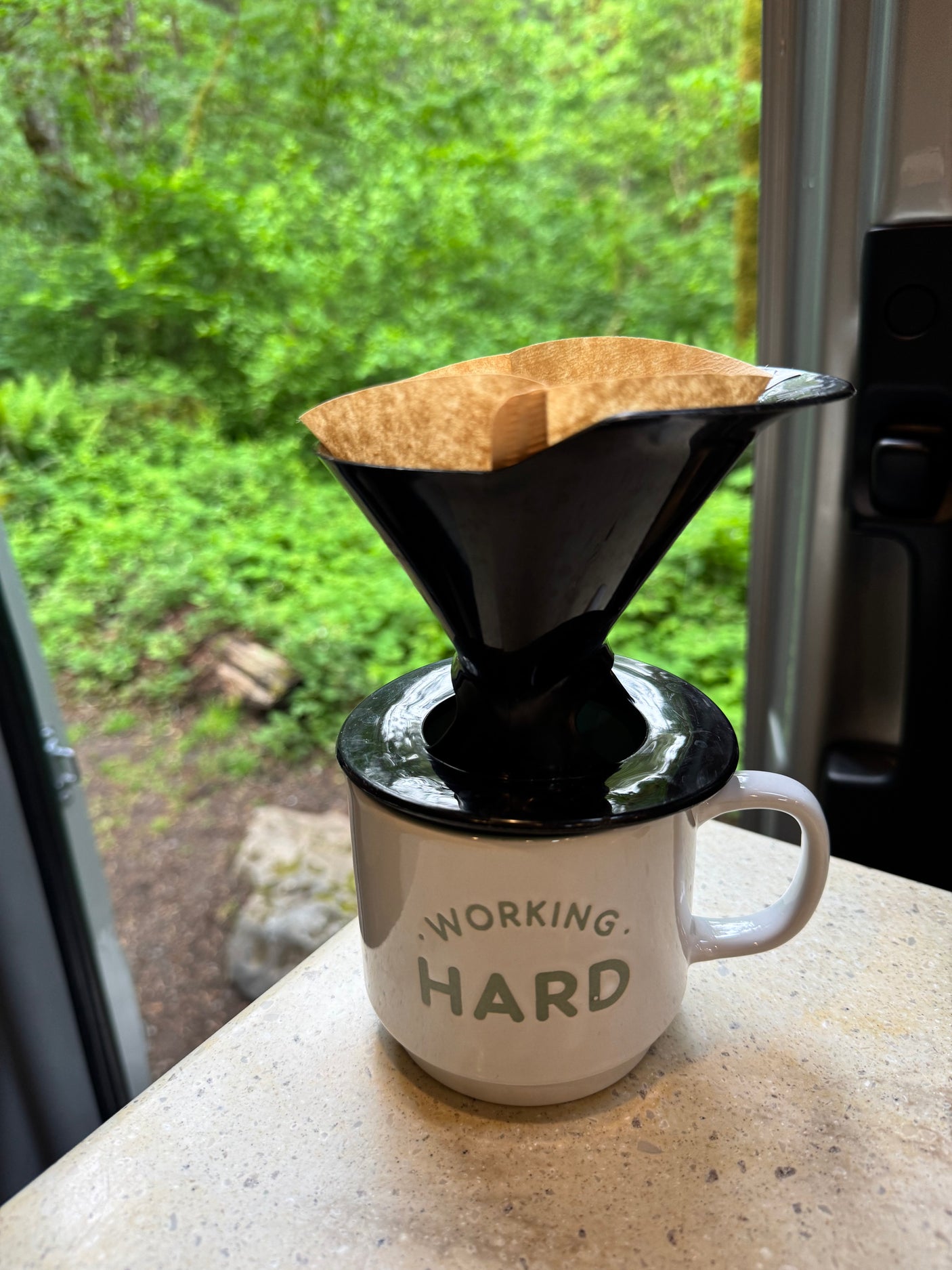 Starting the day with pour-over coffee in an RV rental. "Working Hard" mug, nature view. Perfect for travel & camping.
