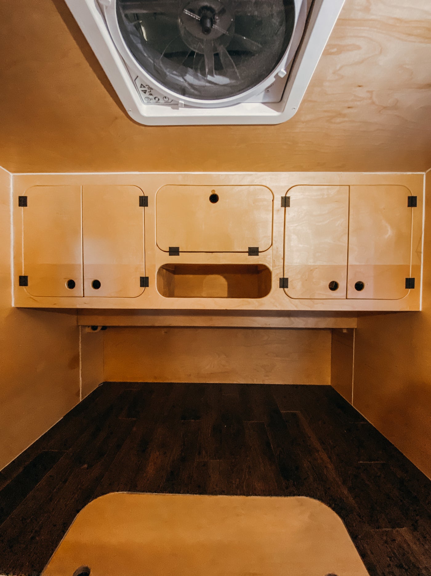 RV rental interior with a ceiling vent, light wood overhead cabinets (some with circular pulls), and a dark wood bed/floor. — photo 6