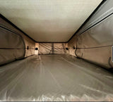 Interior of an RV rental pop-top tent. A clean, plastic-covered mattress forms the sleeping area, ready for your camping adventure.