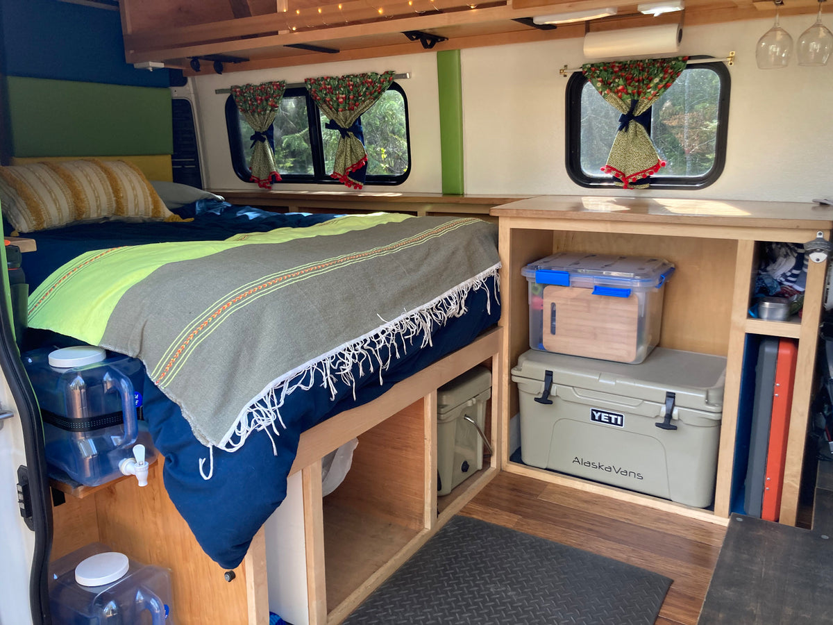 Cozy RV rental camper van interior with a comfortable bed, smart storage solutions, and scenic windows.