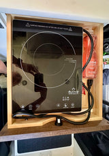 A DUXTOP induction cooktop, with power cord and dish soap, rests in a wooden cubby within an RV rental.