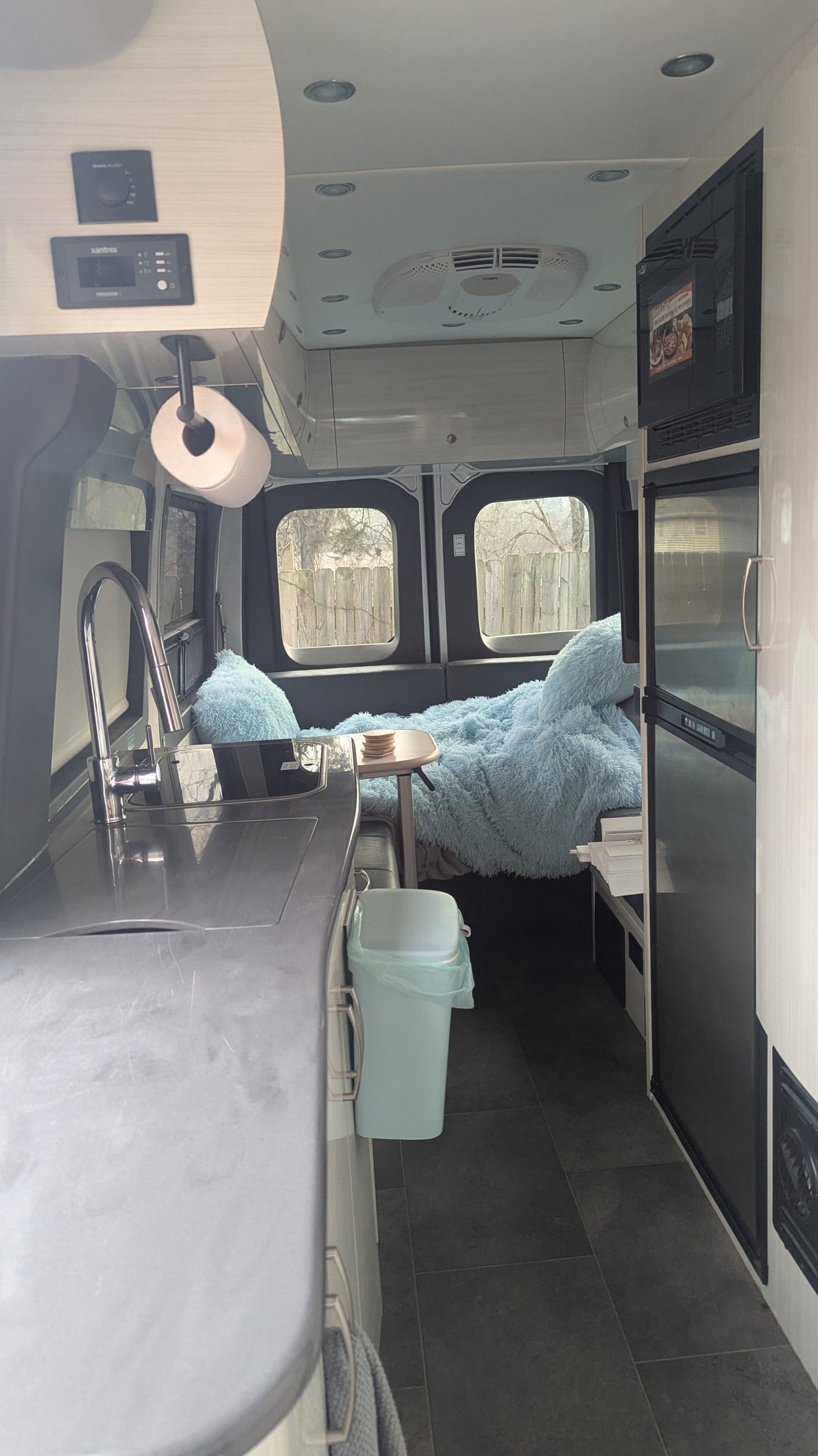 Inside this rv rental van: a well-equipped kitchenette, cozy blue bed, fridge, and overhead controls for comfy travels.