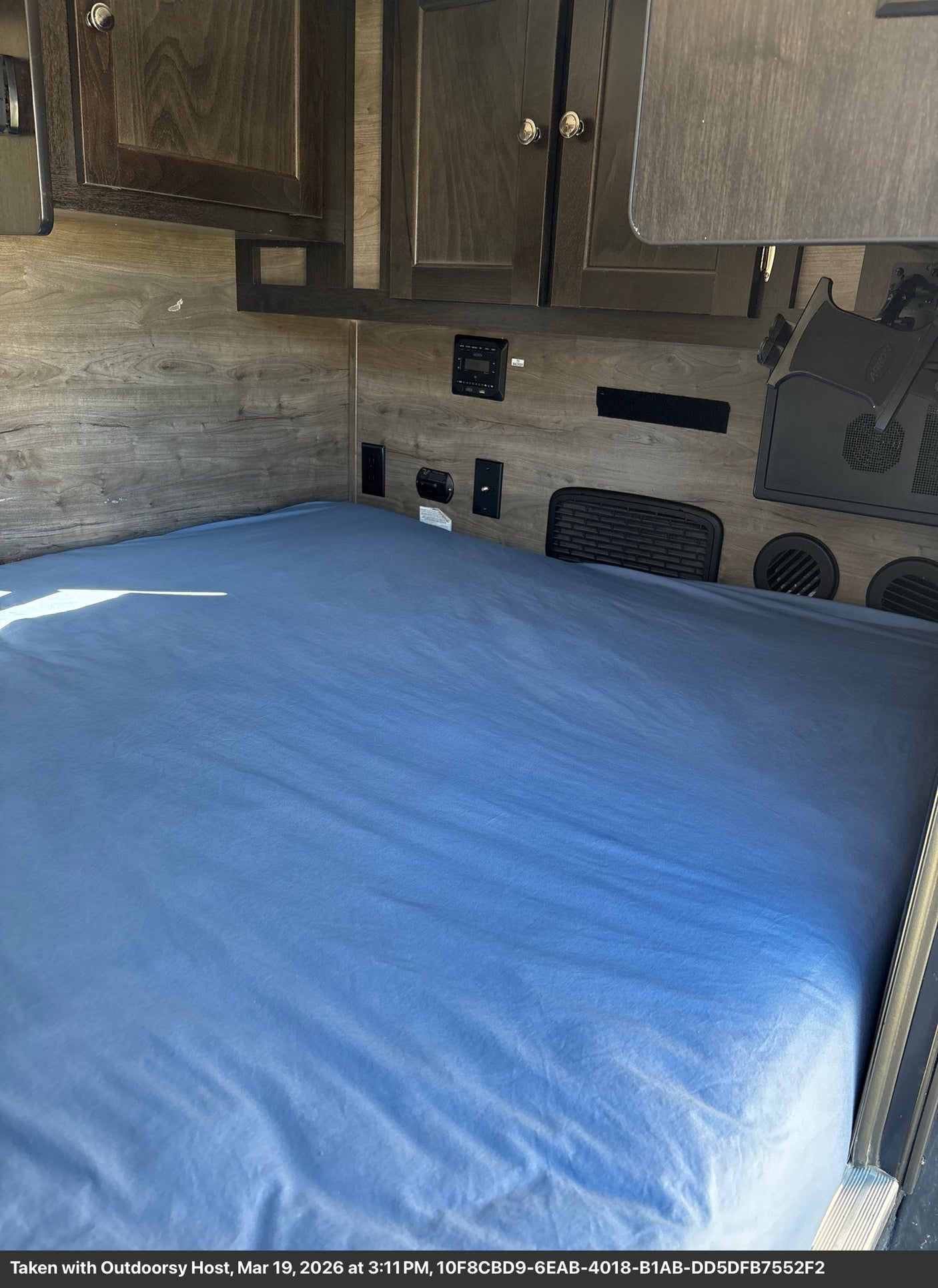 Inside this RV rental: a cozy bedroom with a blue bed, wood walls, overhead cabinets, and built-in amenities.