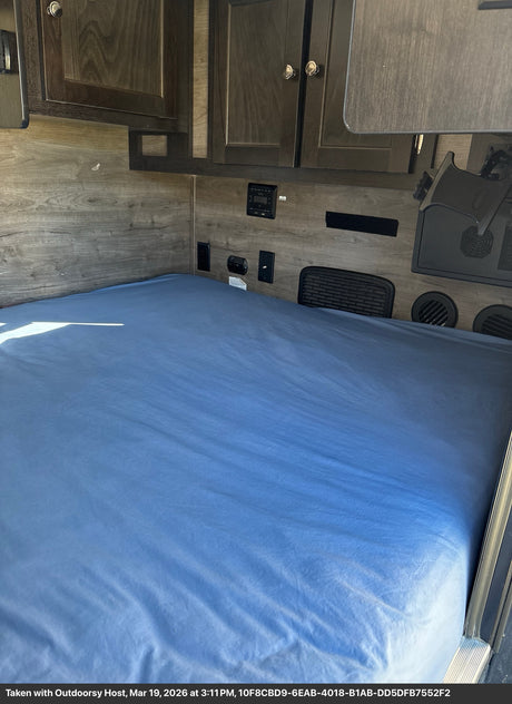 Inside this RV rental: a cozy bedroom with a blue bed, wood walls, overhead cabinets, and built-in amenities.