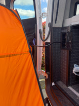 RV rental: An orange outdoor privacy tent extends from the open van door, revealing interior utility hookups & bedding.
