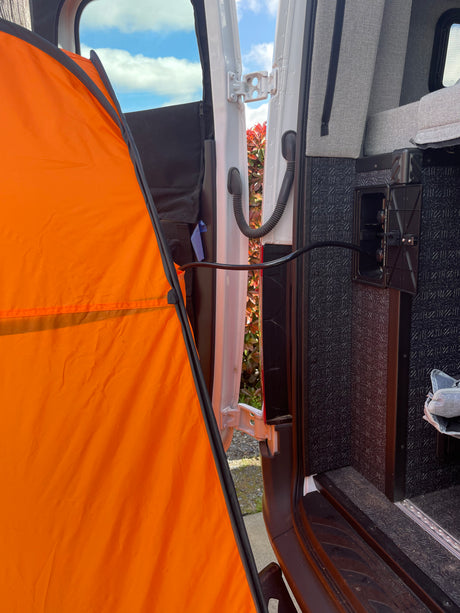 RV rental: An orange outdoor privacy tent extends from the open van door, revealing interior utility hookups & bedding.