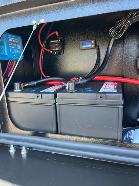 RV rental power setup: Victron solar charge controller, circuit breaker, and batteries inside a rugged black compartment.