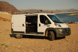 White camper van parked by a lake & mountains, showcasing an RV rental conversion with an open side door.