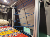 Cozy RV rental interior featuring a bed with a colorful quilt and an innovative bungee cord storage system along the wall.