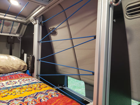 Cozy RV rental interior featuring a bed with a colorful quilt and an innovative bungee cord storage system along the wall.