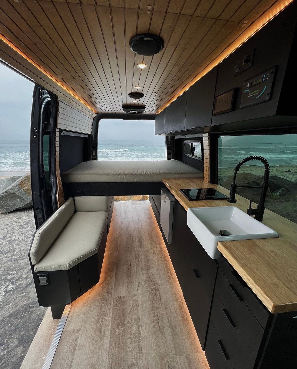 Gorgeous custom camper van interior featuring a full kitchen, bed, & ocean views. Ideal for a luxury RV rental experience.