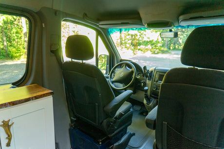 Inside an RV rental: driver's and passenger areas, steering wheel, and a custom wood-top cabinet in this converted van.