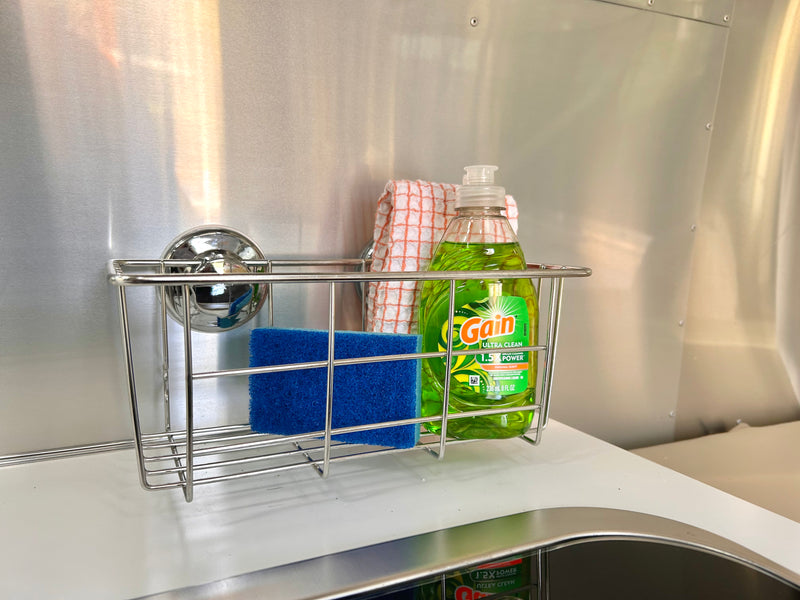 Dish soap, sponge, and towel organized in a suction-cup caddy on the metal wall of an RV rental kitchen. — photo 11
