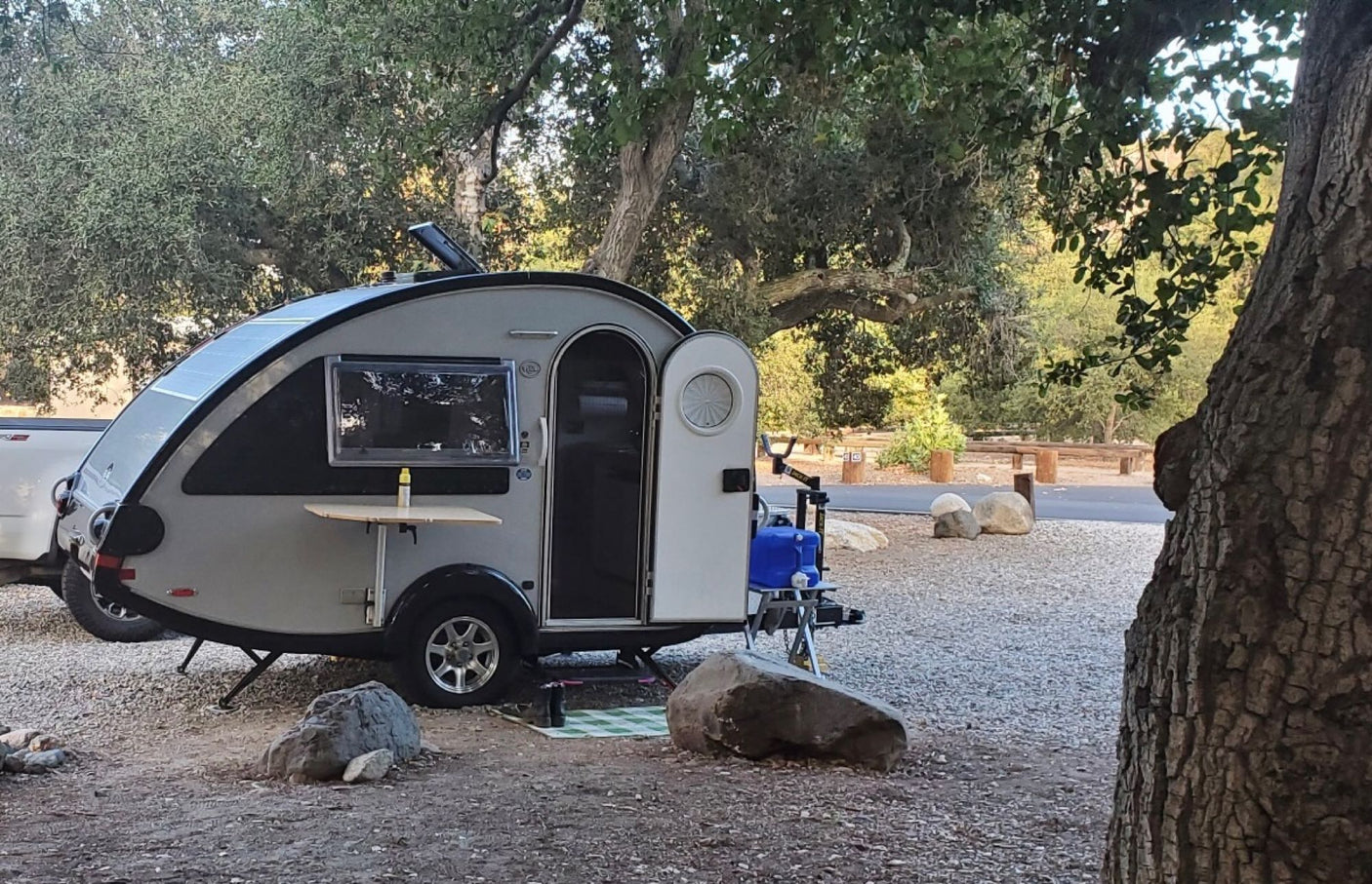 Teardrop RV rental at a leafy campsite, with an open door, side table, and water jug.
