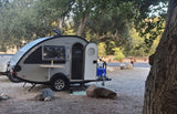 Teardrop RV rental at a leafy campsite, with an open door, side table, and water jug.