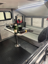 Experience cozy dining in this RV rental's modern interior. Complete with table, seating, and ambient lighting.