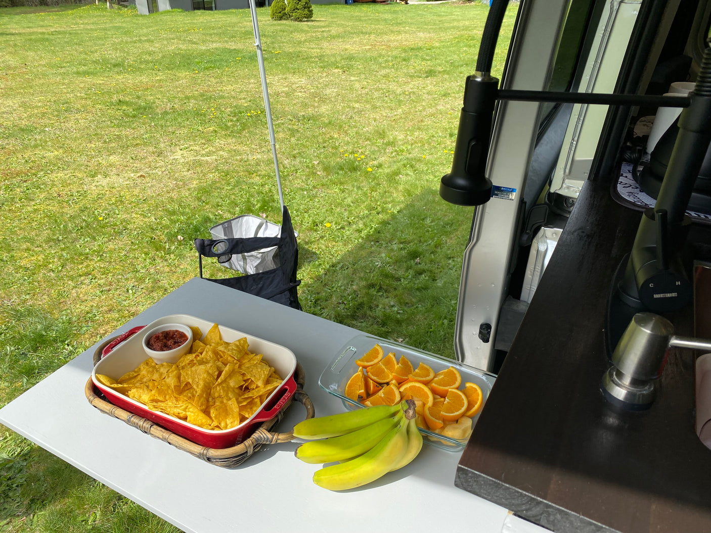 Outdoor snacks: chips, salsa, fruit, and bananas on a table next to an RV rental, enjoying nature.