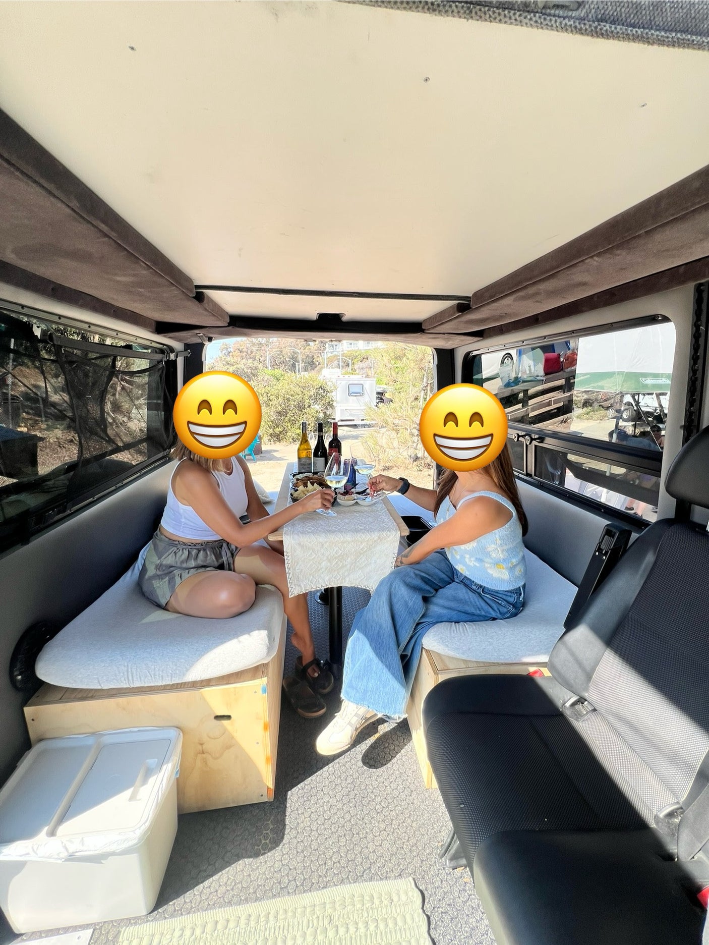 An RV rental's inviting interior: Two women toast with wine and snacks in a comfy camper van, perfect for mobile dining.