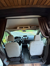RV rental van interior from rear, showing driver & passenger seats, dashboard view, wooden ceiling, and dark privacy curtains.