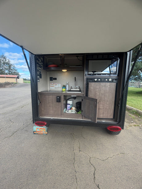 This RV rental's compact outdoor kitchen features a sink, microwave, fridge, and storage for camping essentials.