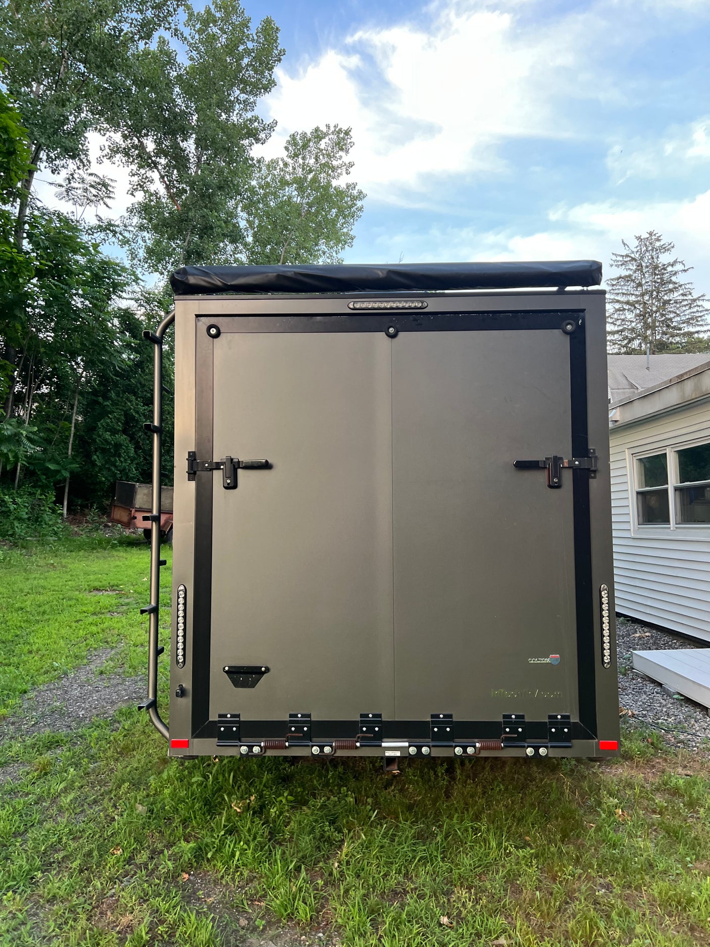 Rugged, dark grey adventure cargo trailer with rooftop tent and ladder, perfect for RV rental and outdoor exploration.