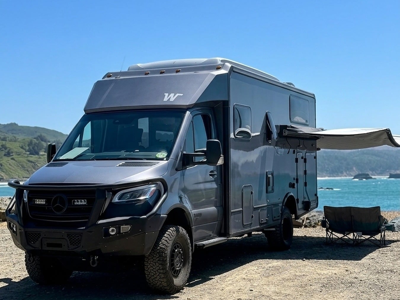  ready for adventure among towering pine trees.|Grey EKKO rv rental parked at a tranquil mountain campsite with a picnic table — photo 4