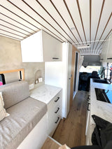 Inside a sleek rv rental, showing its modern kitchen, comfy seating, and bright, wood-accented ceiling.