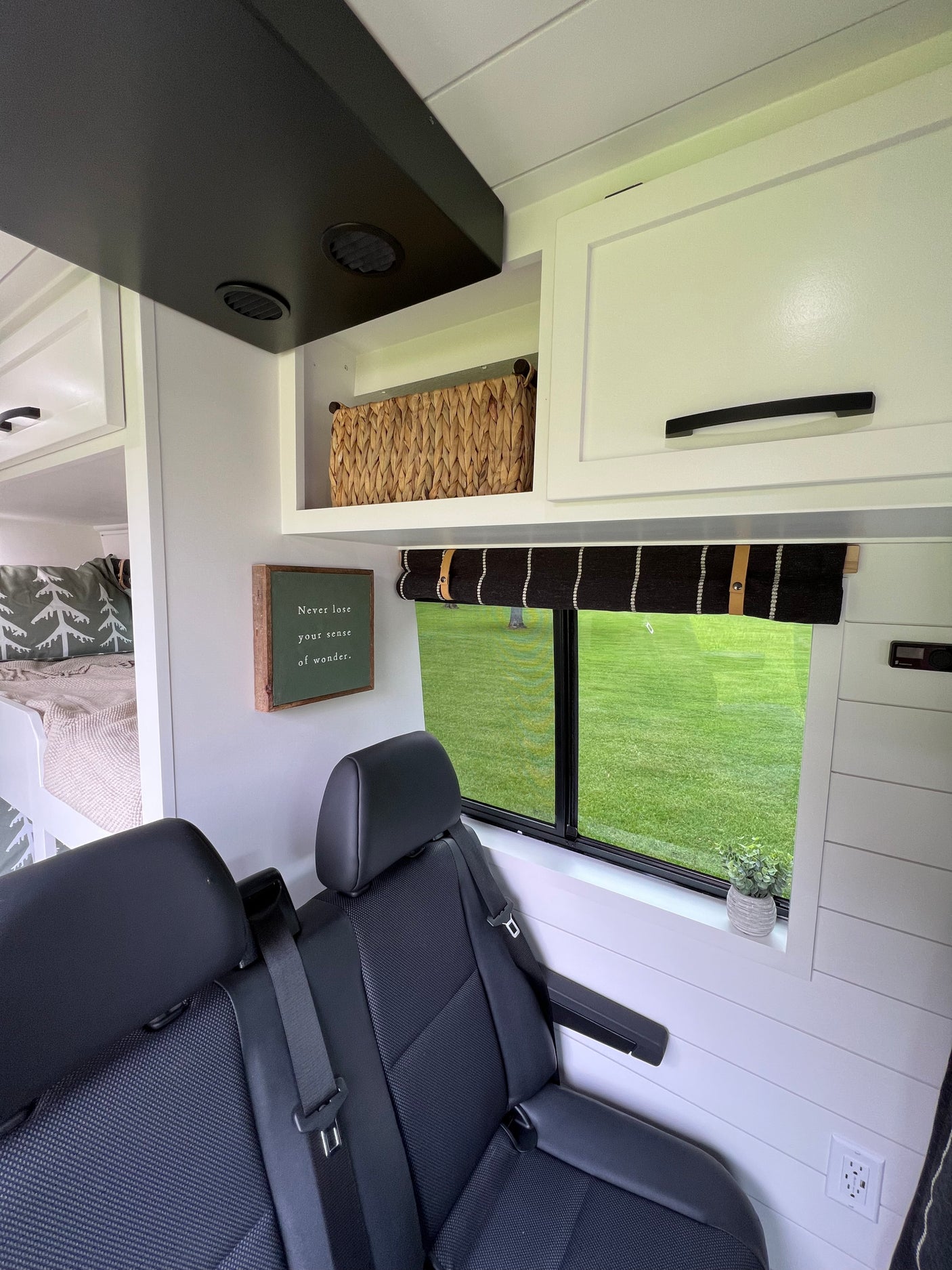 Modern RV rental interior: bunk beds, comfy passenger seats, overhead storage, and window view of green landscape.