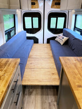 RV rental interior featuring blue sofa seating, convertible wooden floor bed, and practical counter space for comfortable travel.