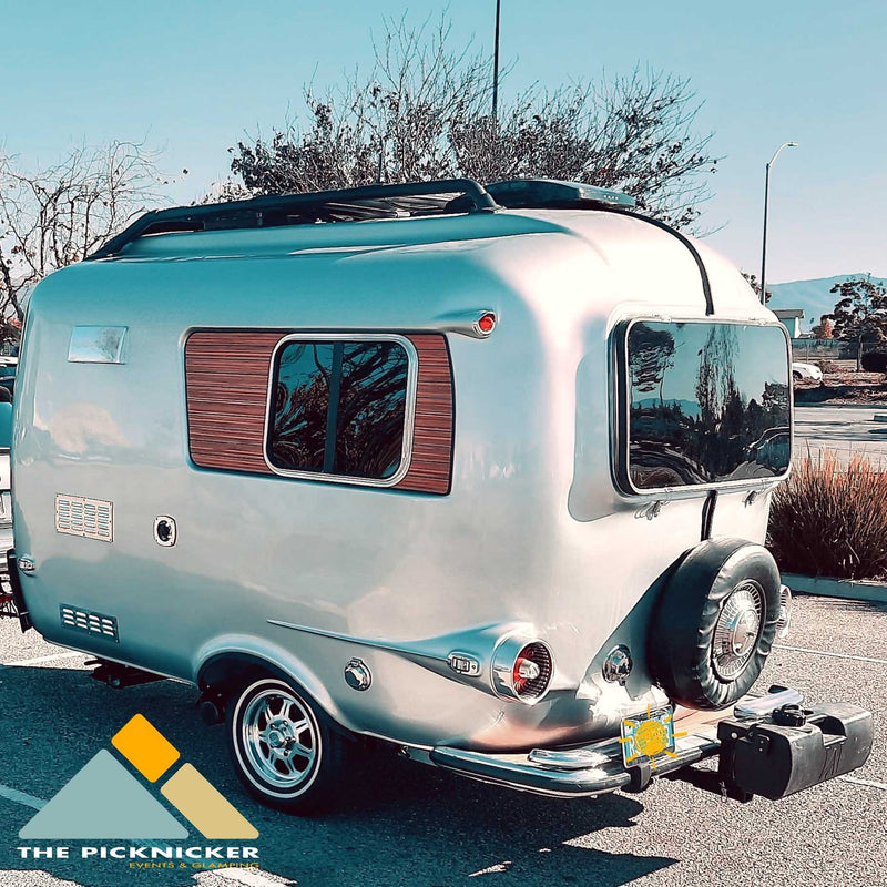 Vintage silver RV rental: Rear view of a stylish travel trailer with chrome details & spare tire, parked outdoors. — photo 15