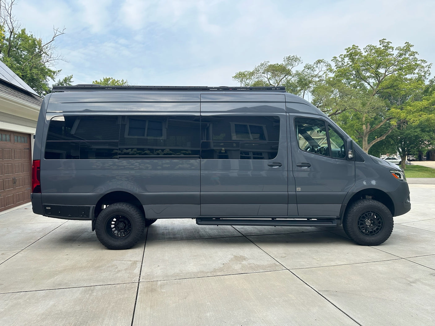 A full side view of a custom dark grey adventure van with a roof rack & off-road tires, great for an RV rental.