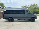 A full side view of a custom dark grey adventure van with a roof rack & off-road tires, great for an RV rental.
