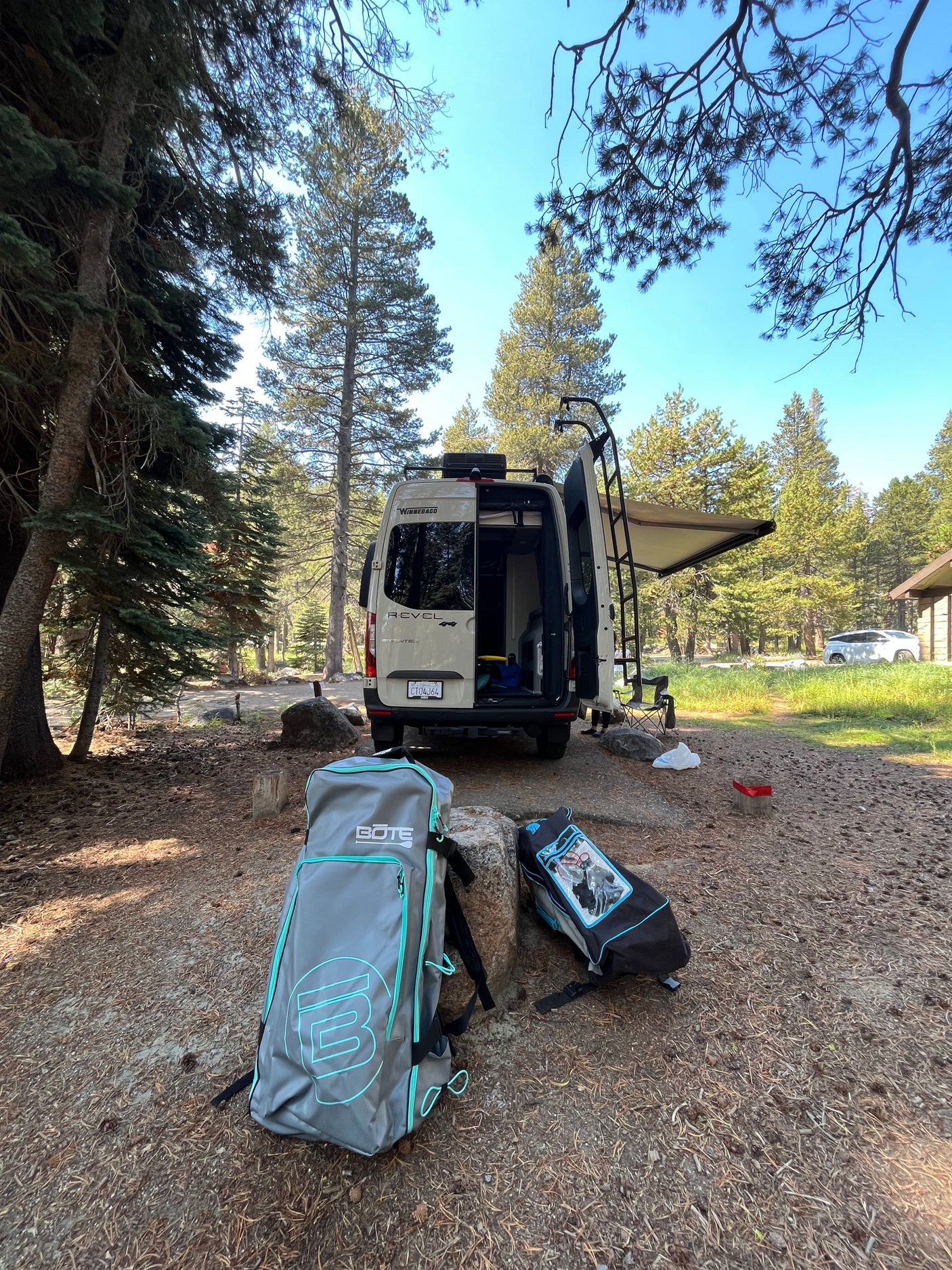 Winnebago Revel RV rental set up at a sunny forest campsite with adventure gear on the ground.