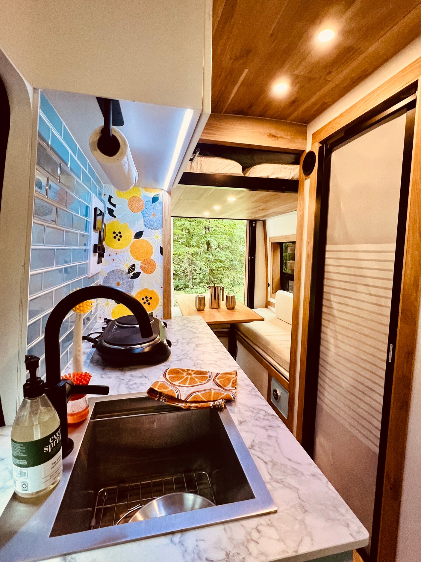 RV rental interior: stylish kitchen with marble counters, sink, and dining area with forest views.