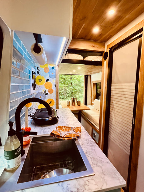 RV rental interior: stylish kitchen with marble counters, sink, and dining area with forest views.