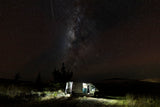 Experience epic stargazing nights with an RV rental. A campervan glows under the Milky Way in a serene, dark landscape.