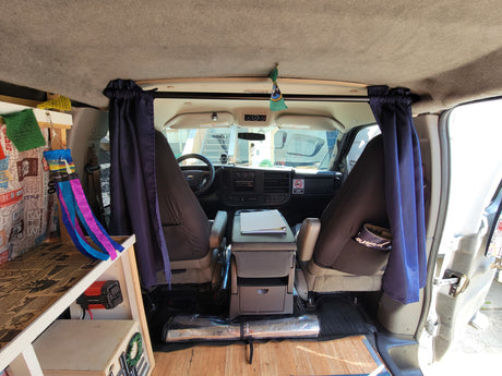 Cozy rv rental camper van interior. View from back showing custom built-ins, privacy curtains & dashboard.