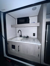 Inside an RV rental: a compact kitchen with sink, microwave, and refrigerator for convenience.