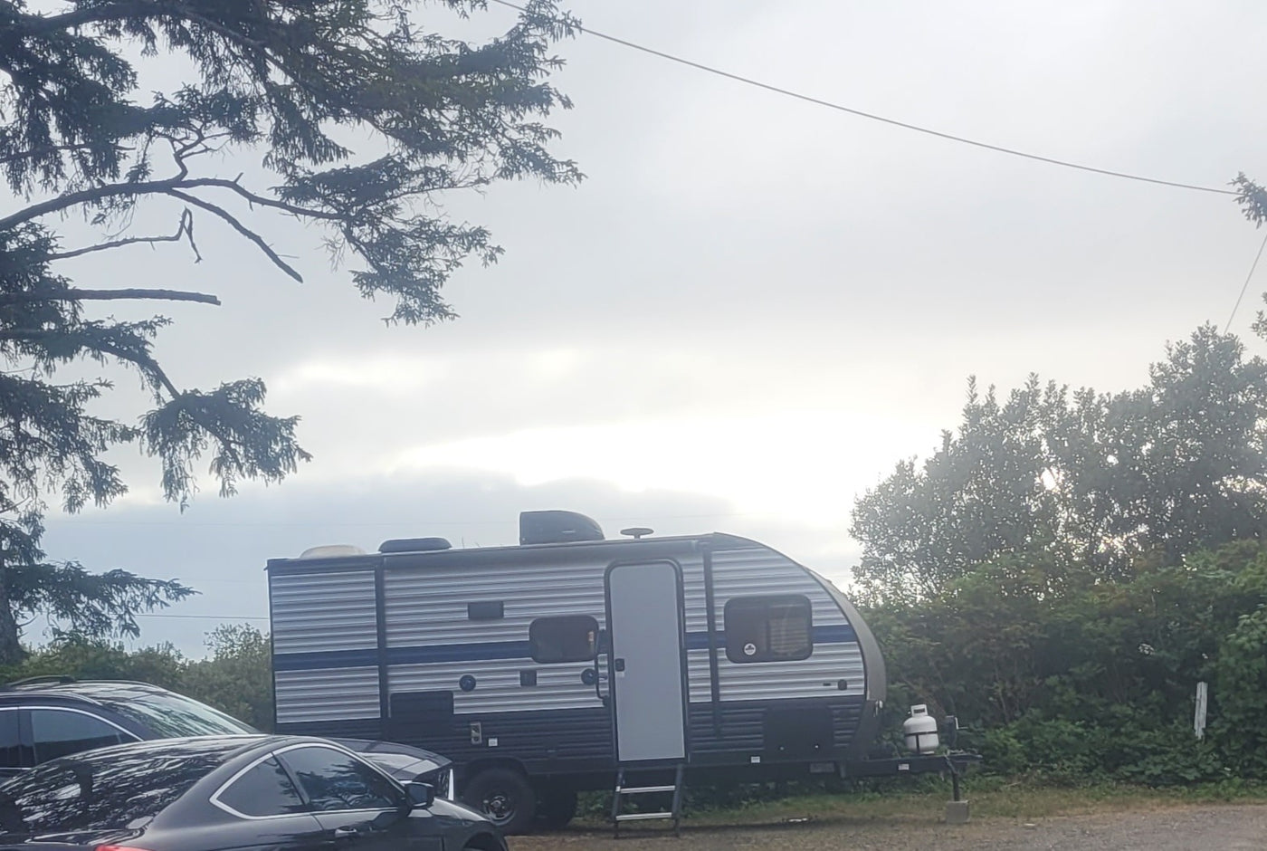 An RV rental travel trailer is parked outdoors under an overcast sky, with cars and trees nearby. Ready for camping!