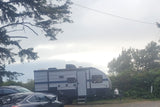 An RV rental travel trailer is parked outdoors under an overcast sky, with cars and trees nearby. Ready for camping!
