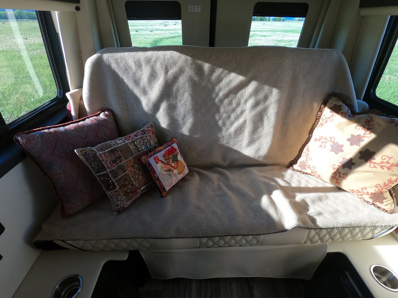 Cozy RV rental interior featuring a sofa with decorative pillows, sunlight, and a scenic view of green fields through the windows. — photo 12