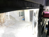 RV rental: View from inside, looking through a zippered mesh screen at an outdoor building & cooler. Interior bed seen right.