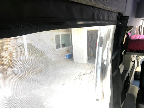 RV rental: View from inside, looking through a zippered mesh screen at an outdoor building & cooler. Interior bed seen right.