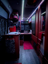 Cozy RV rental interior features dark wood cabinetry, a compact kitchen, workspace, & bright LED lighting.