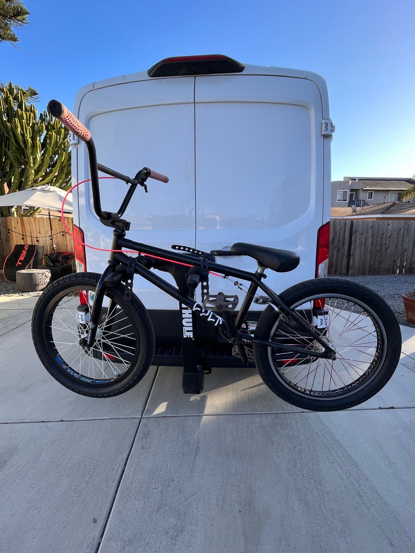 A black BMX bike with pink handles is mounted on a Thule rack at the back of a white van, ready for an RV rental trip. — photo 20