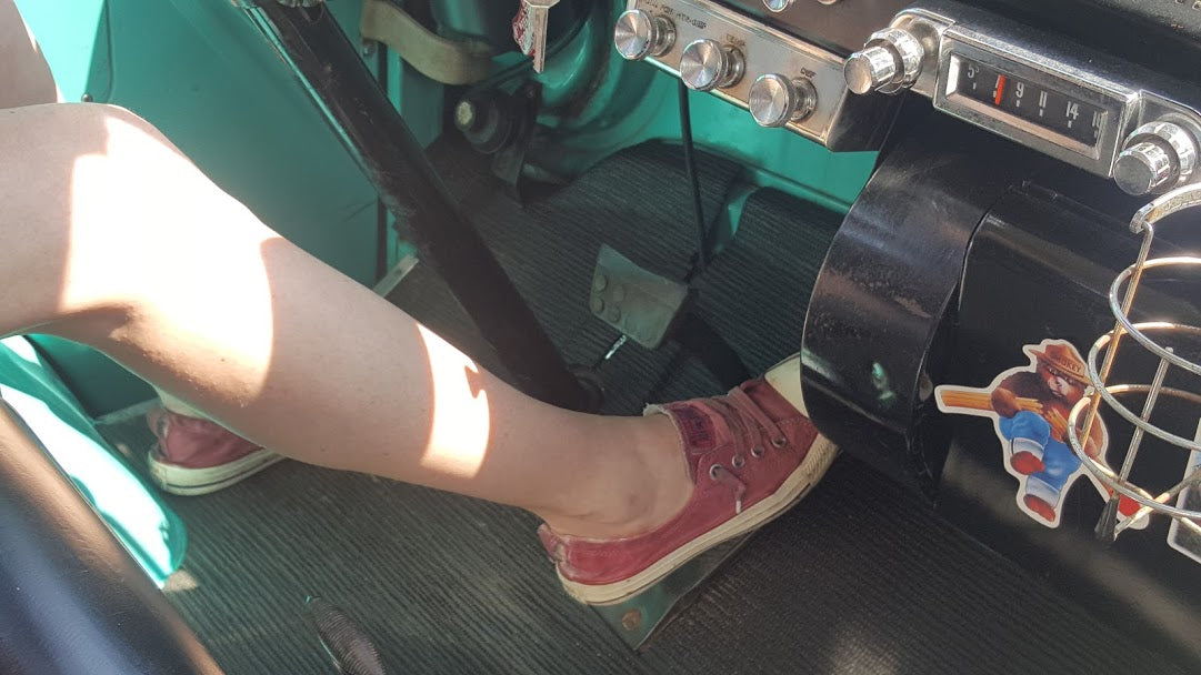Leg in red shoe pressing gas pedal in a vintage RV rental. Dashboard features an old radio and Smokey Bear sticker.