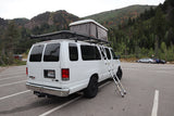 Explore nature with this white rv rental camper van, featuring a rooftop tent & ladder, parked by autumn mountains.