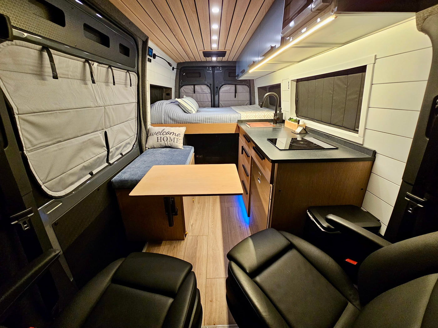 Inside this RV rental: a cozy camper van with kitchen, bed, dining, and driver seats in a modern design. — photo 10