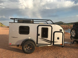 MAX Flyer RV rental, a compact travel trailer with roof rack, parked by a lake. Perfect for your next camping adventure.