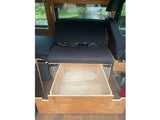 RV rental: Open wooden drawer beneath black padded seating with seatbelts, offering a glimpse of the outdoor scenery.